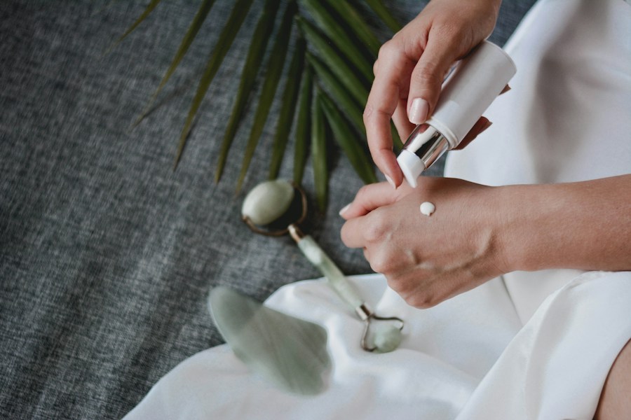 Mãos aplicando creme ao lado de um rolinho de jade e uma folha de palmeira