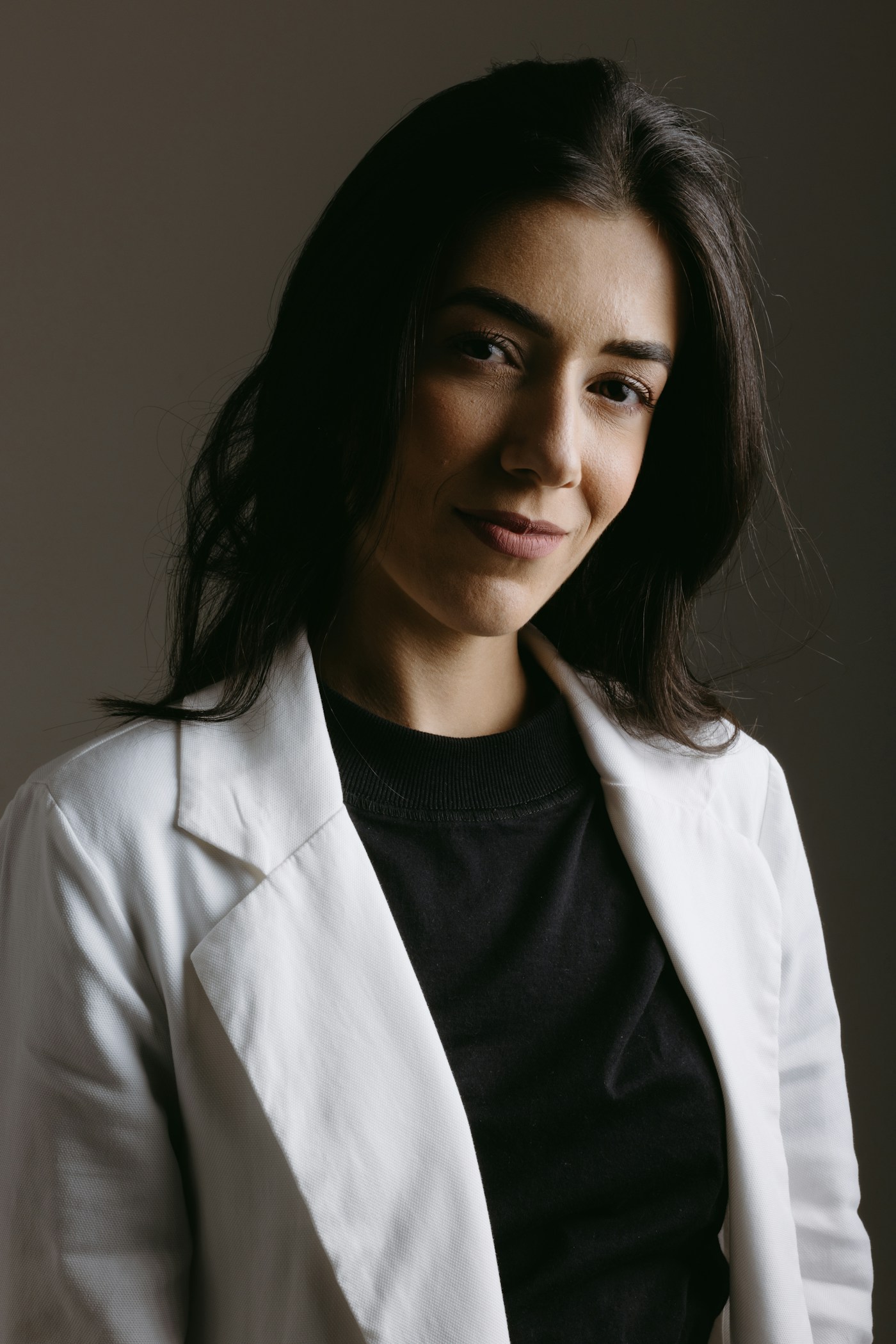 Retrato de Clara Menezes, de blazer claro, em fundo escuro